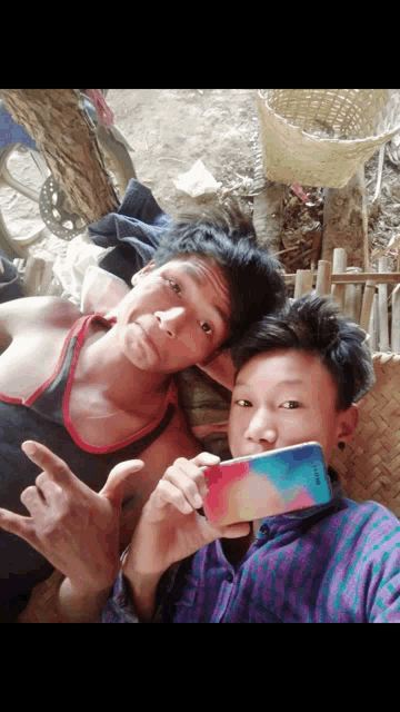 two young men are posing for a picture and one is holding a phone that says samsung