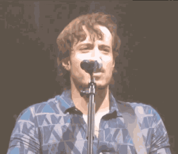 a man singing into a microphone while wearing a blue shirt with the letter x on it