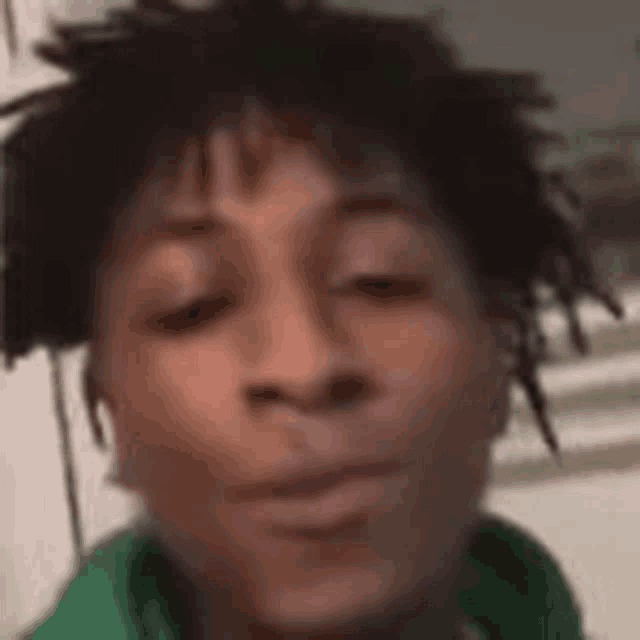 a young man with dreadlocks is wearing a green shirt and looking at the camera .