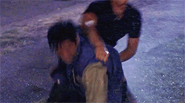 a man is holding another man 's back while standing in the rain .