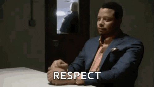 a man in a suit is sitting at a table with his hands folded and the word respect written on the screen .
