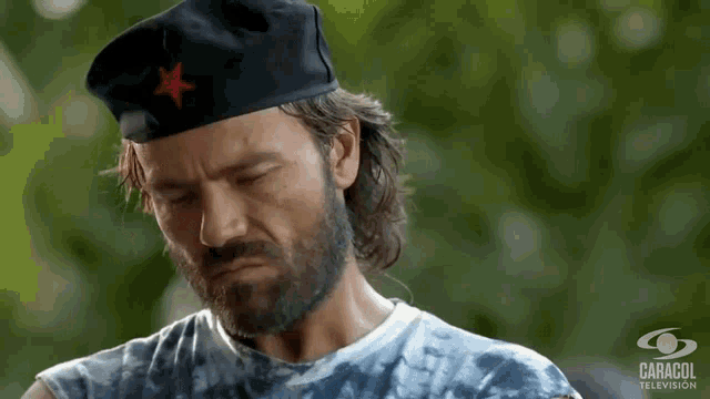 a man with a beard wears a black hat with a red star