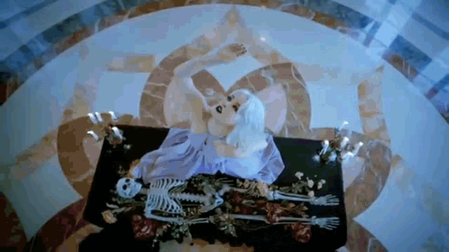 a woman in a purple dress is laying on a table with a skeleton .