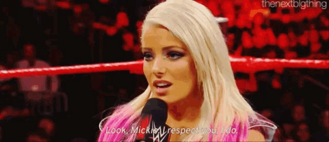 a woman is talking into a microphone in a wrestling ring while standing in front of a crowd .