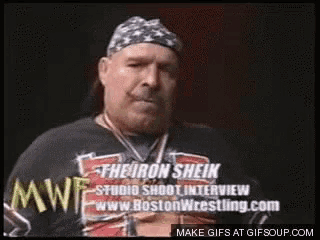 a man with a beard and a bandana on his head is wearing a boston wrestling shirt .