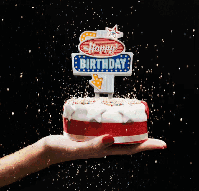 a woman holds a small birthday cake with a happy birthday sign on top