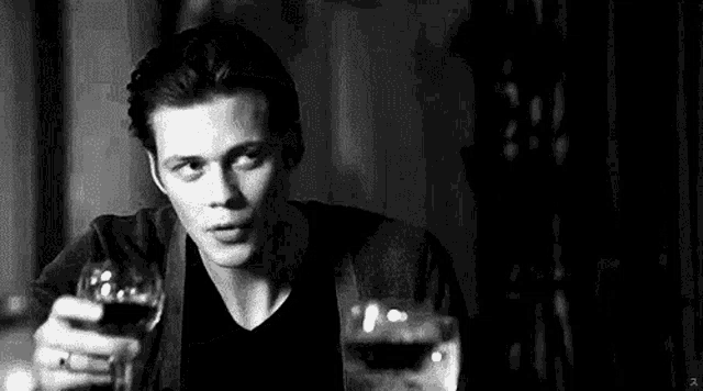 a man is sitting at a table holding a glass of wine and a glass of water .
