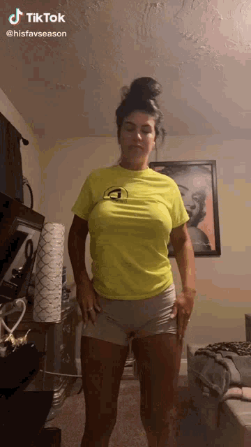 a woman in a neon yellow shirt and grey shorts is standing in a living room .