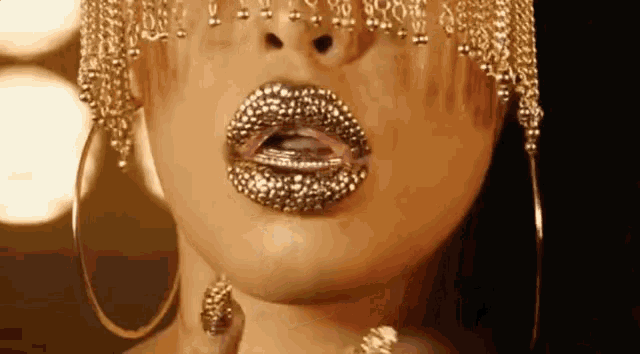 a close up of a woman 's mouth with gold lipstick and earrings .