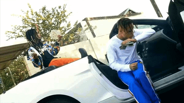 a man in a white shirt is sitting in a white car while another man holds a bunch of money