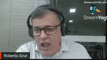 a man wearing headphones and glasses is sitting in front of a computer screen .