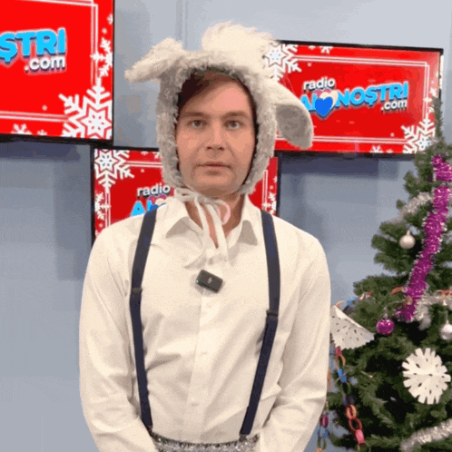 a man wearing bunny ears and suspenders stands in front of a christmas tree in front of a sign that says radio nostri