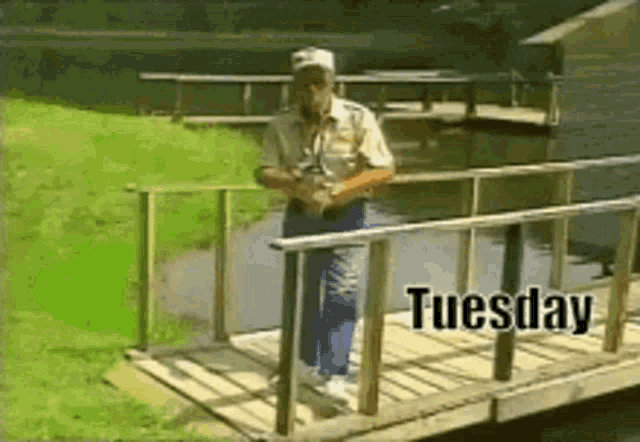a man standing on a wooden bridge with the date tuesday written on it