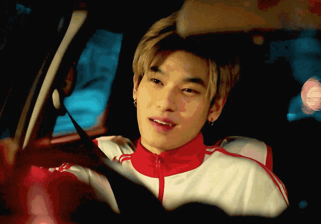 a young man wearing a red and white jacket is driving a car