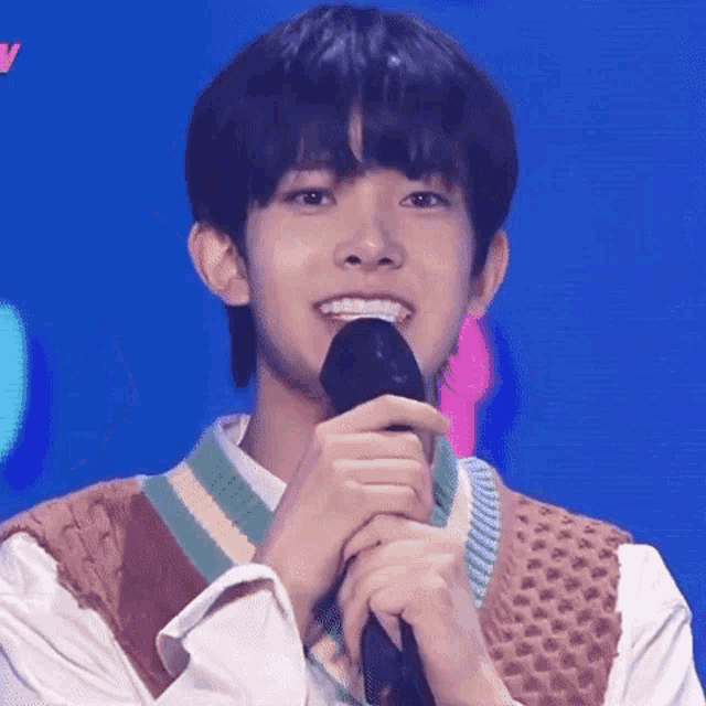 a young man is smiling while holding a microphone in his hand .