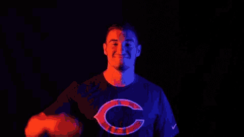 a man wearing a chicago bears shirt is making a peace sign in the dark .