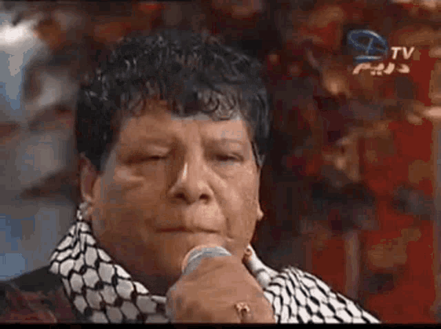 a man is singing into a microphone while wearing a scarf and a ring .
