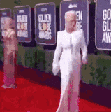 a woman in a white dress is standing on a red carpet at a golden globe awards event .