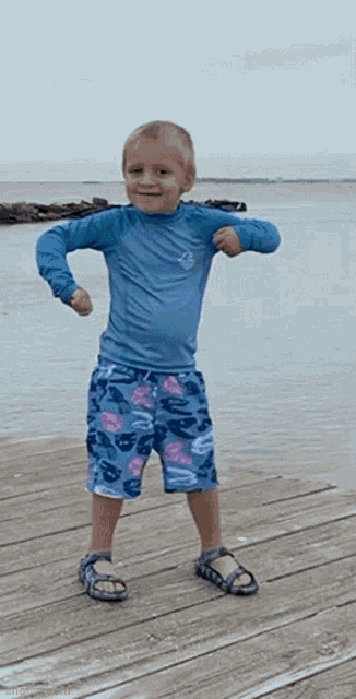 a young boy in a blue shirt and shorts stands on a dock