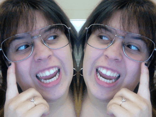 a woman wearing glasses and a ring is smiling in a mirror