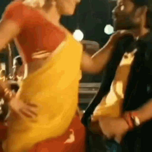 a man is holding a woman 's waist while she is dancing in a yellow saree .