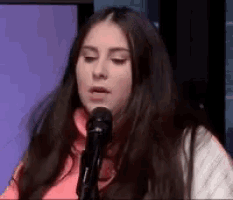 a woman is singing into a microphone while wearing a pink shirt .