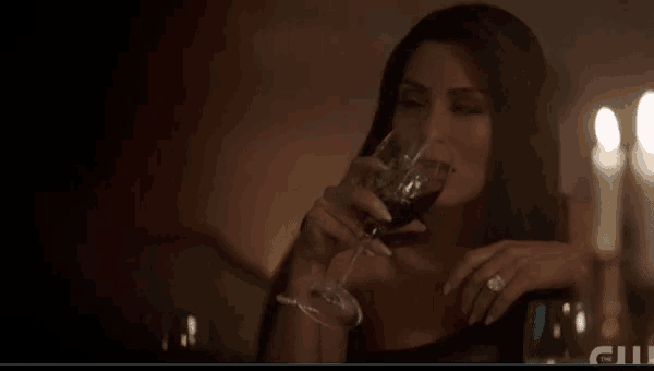 a woman is drinking a glass of wine while sitting at a table with candles .