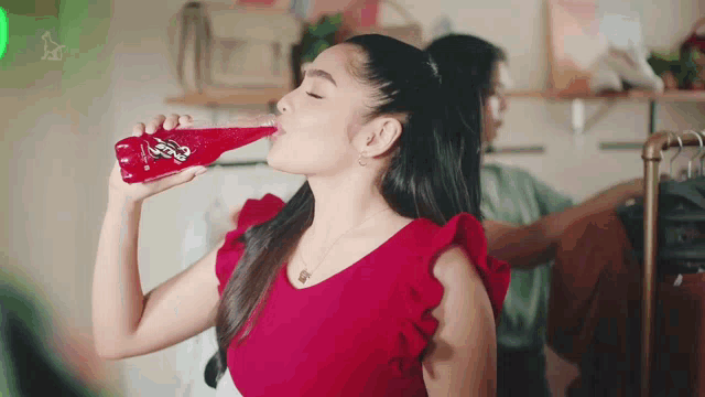 a woman in a red top drinks from a bottle of sprite