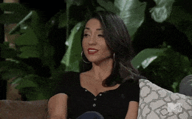 a woman is sitting on a couch with a pillow in front of a plant .