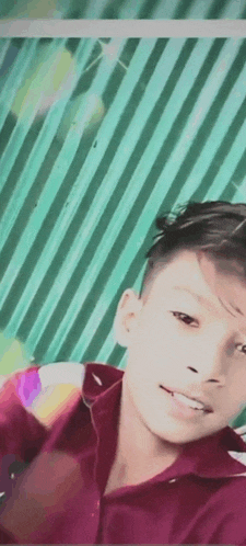 a young boy in a red shirt is taking a selfie in front of a green striped wall .