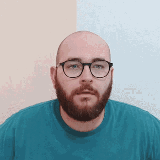 a bald man with glasses and a beard wears a blue shirt