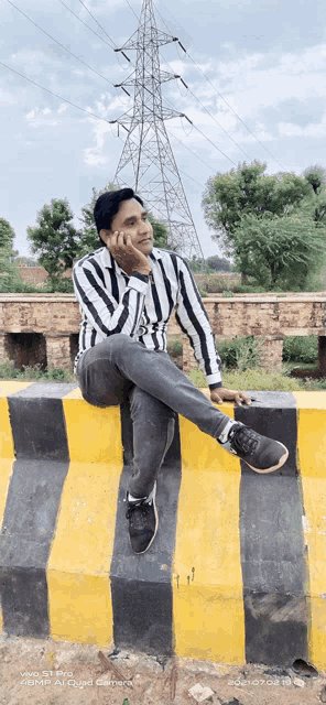 a man sits on a yellow and black striped barrier with a phone that says vivo on it
