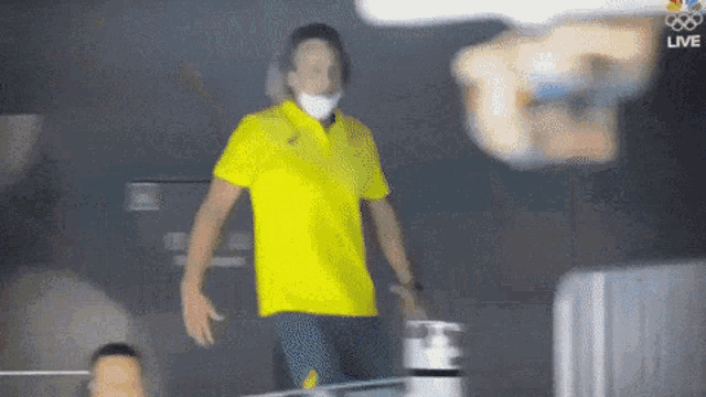 a man wearing a yellow shirt and a face mask is walking in a dark room