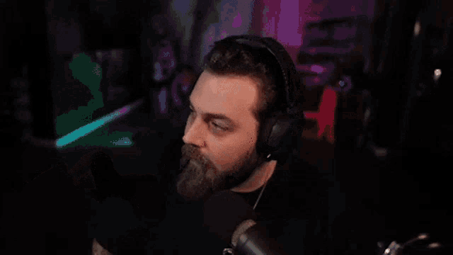 a man with a beard wearing headphones is dancing in front of a microphone in a dark room .