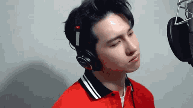 a young man wearing headphones and a red shirt is standing in front of a microphone .