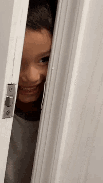 a young boy is peeking out from behind a door .