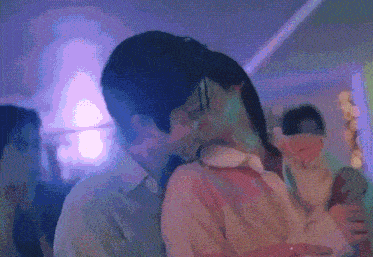 a man and woman are kissing in a room with purple lights behind them