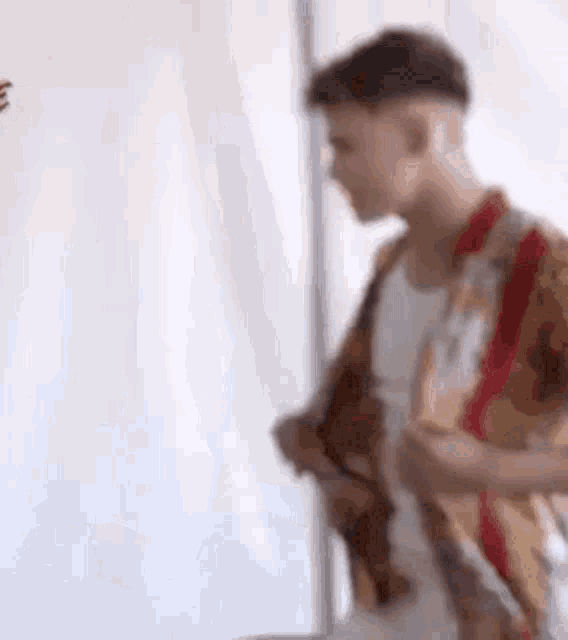 a man in a plaid shirt is standing in front of a white wall .