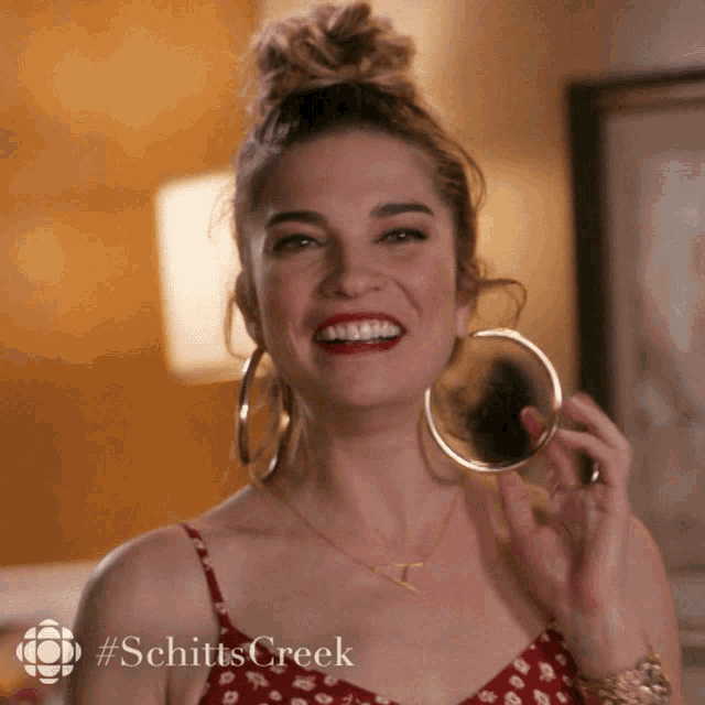 a woman is smiling and holding a mirror with #schitts creek on the bottom right