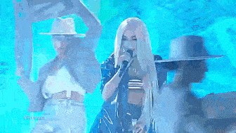 a woman is singing into a microphone on a stage in front of a crowd .