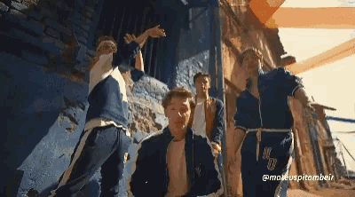 a group of young men are dancing in front of a blue wall and a sign that says @maeuspitombeir