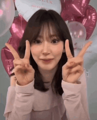 a young woman is giving a peace sign in front of balloons .