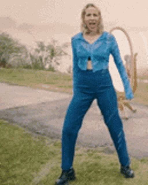a woman in a blue shirt and blue pants is standing on one leg in the grass .