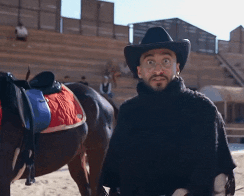 a man wearing a cowboy hat stands in front of a horse