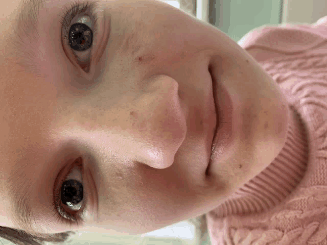 a close up of a person 's face with a pink sweater