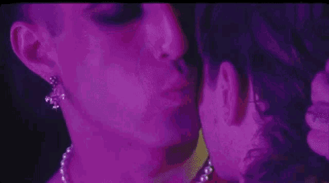 a man and a woman are kissing in a dark room in a purple light .