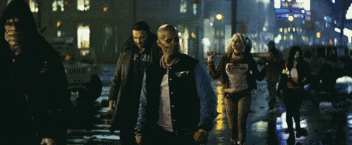 a group of people are walking down a street and one of them is wearing a shirt that says " suicide squad "