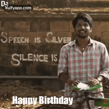 a man is riding a bike in front of a sign that says `` speech is silver , silence is happy birthday ''