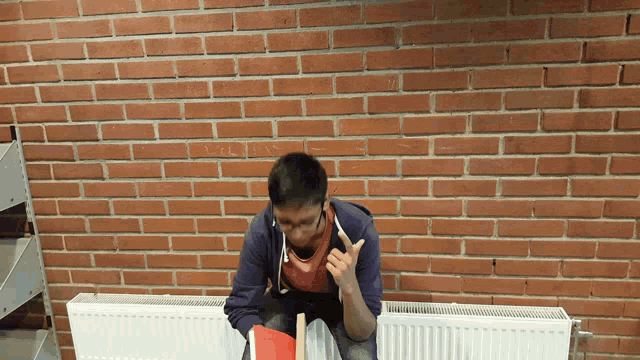 a man sitting in front of a red brick wall talking on a cell phone
