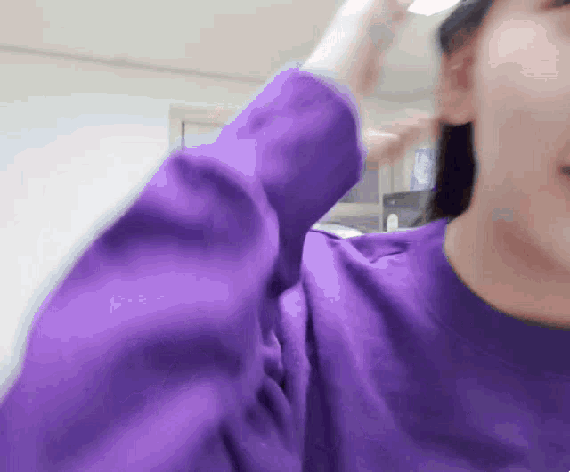 a woman in a purple sweater is holding her hair up
